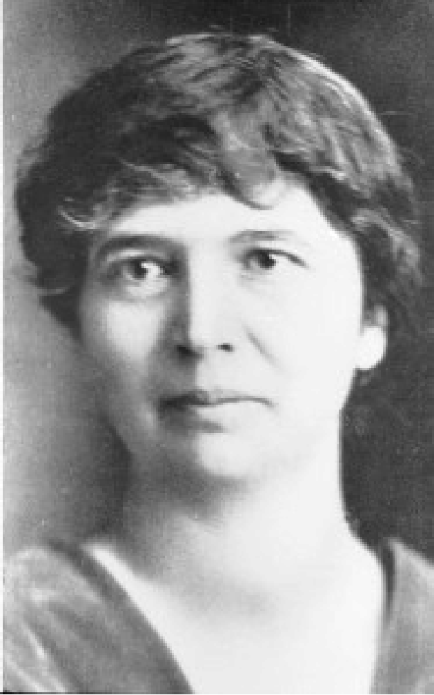 Portrait of Dr. Geneva Misener, a middle-aged white woman with dark hair with bangs, wearing a v-neck top.