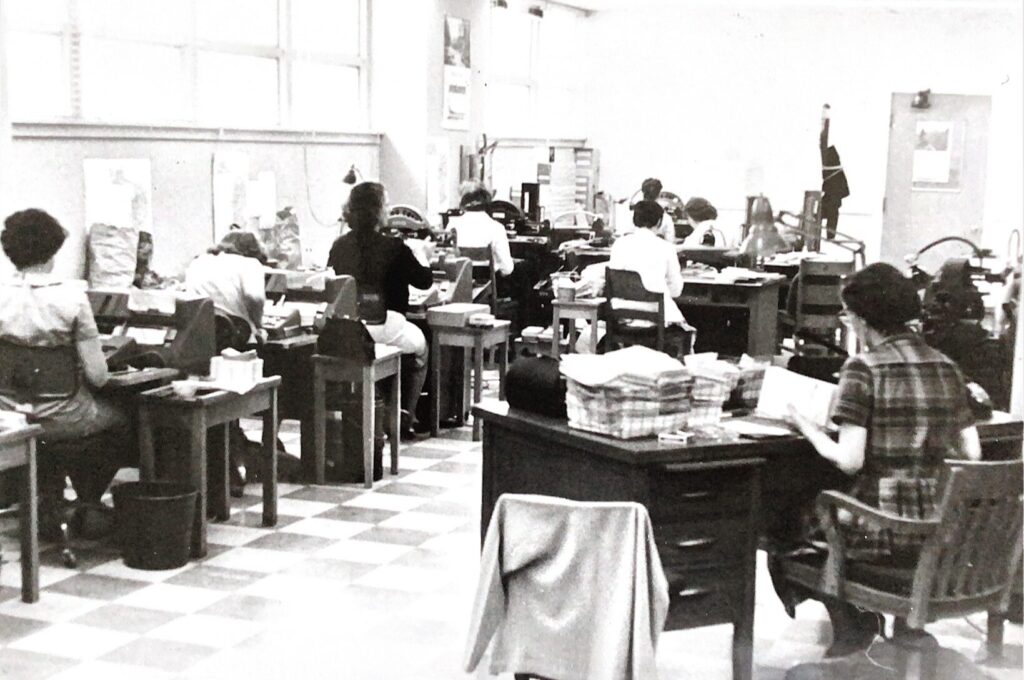 Women workers entering data with key punch machines in a row of workstations. A supervisor sits at a desk in the foreground.