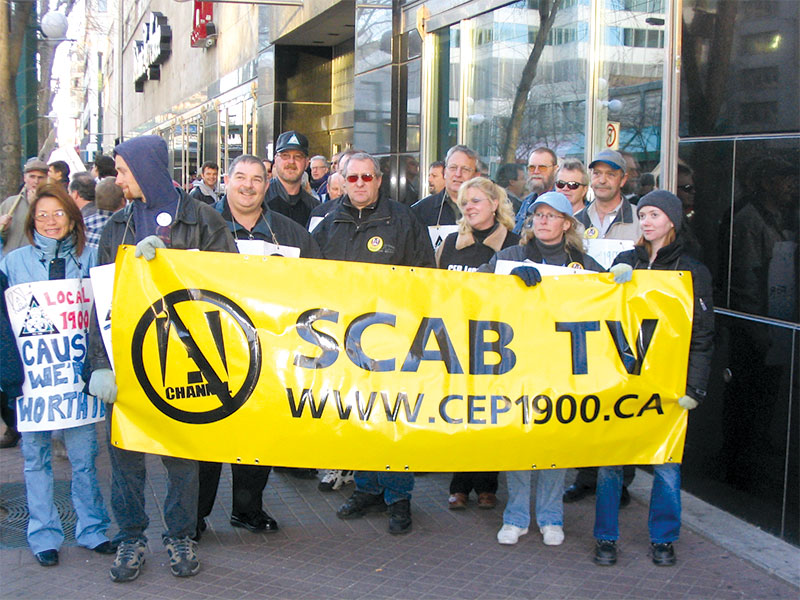 A group of workers standing outside the A-Channel headquarters, holding a sign that says "Scab TV"