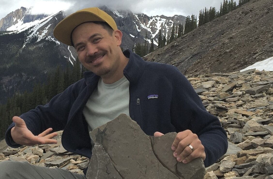 A photo of Chris Chang-Yen Phillips on the slope of Mount Stephen, showing off one of the Burgess Shale fossils.