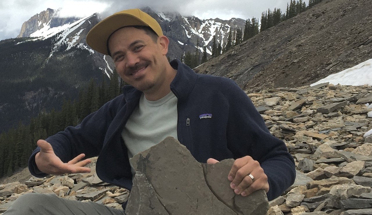 A photo of Chris Chang-Yen Phillips on the slope of Mount Stephen, showing off one of the Burgess Shale fossils.