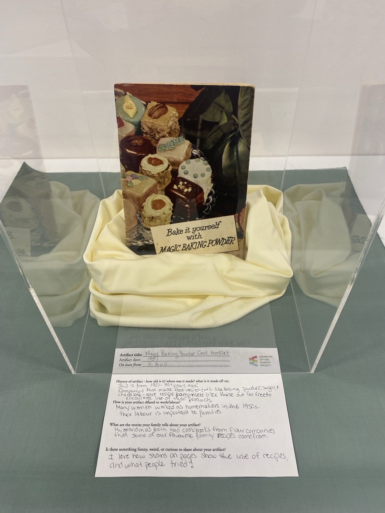 A photo of a cookbook titled "Bake it yourself with MAGIC BAKING POWDER" in a display case