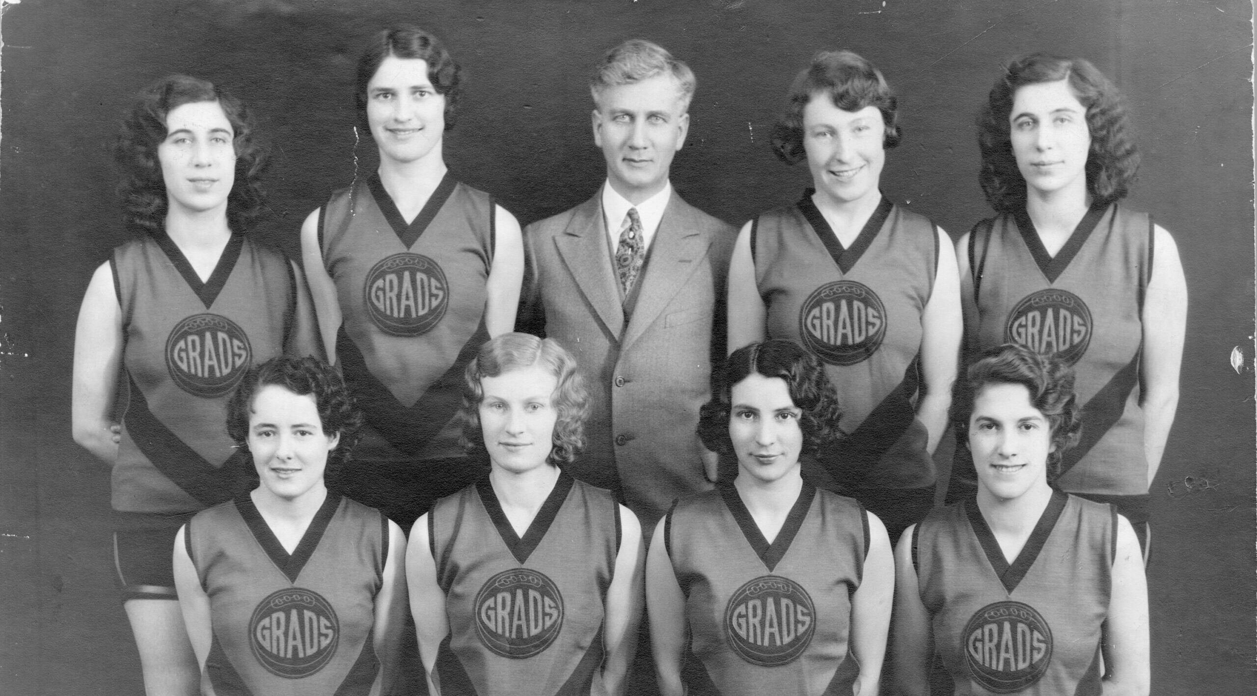 Eight players pose for the camera in their jerseys, with their coach and a basketball.