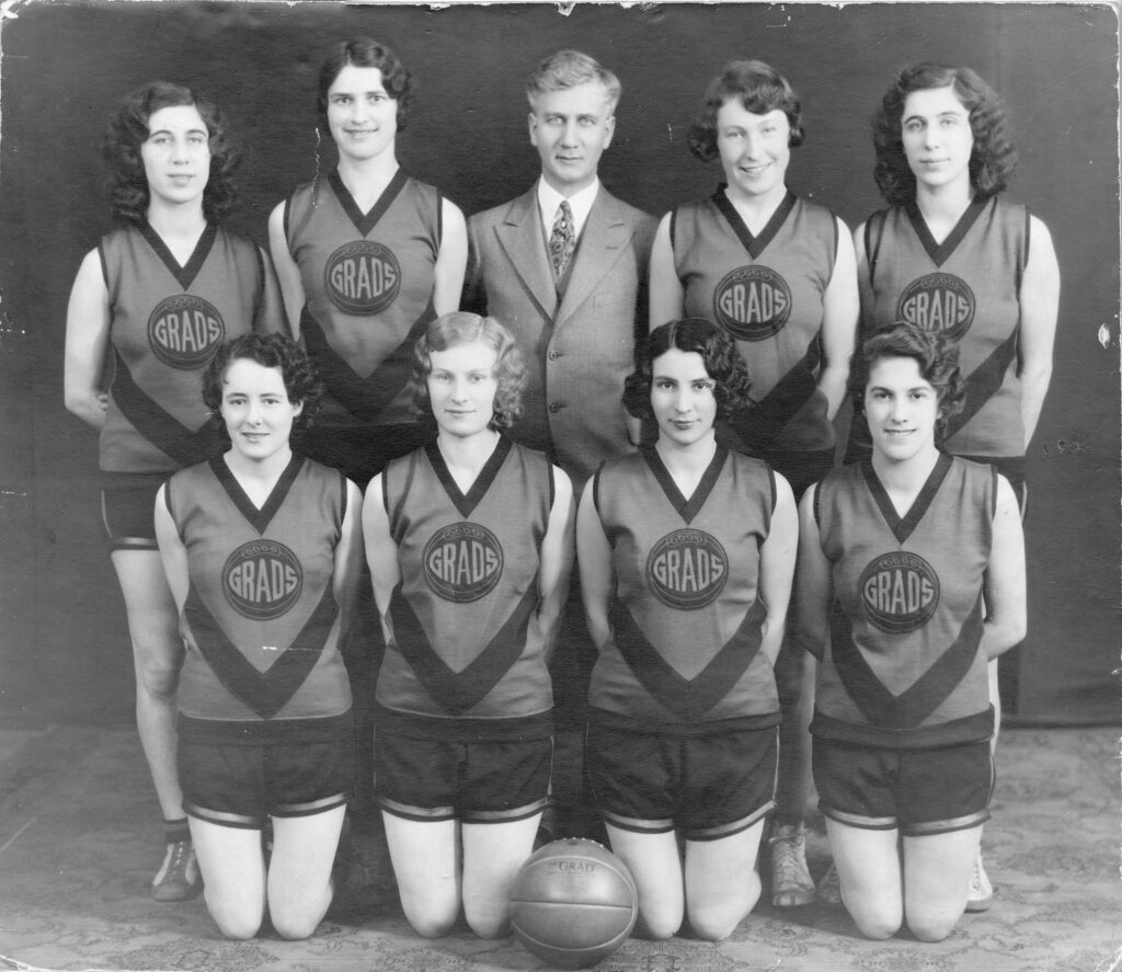 Eight players pose for the camera in their jerseys, with their coach and a basketball.