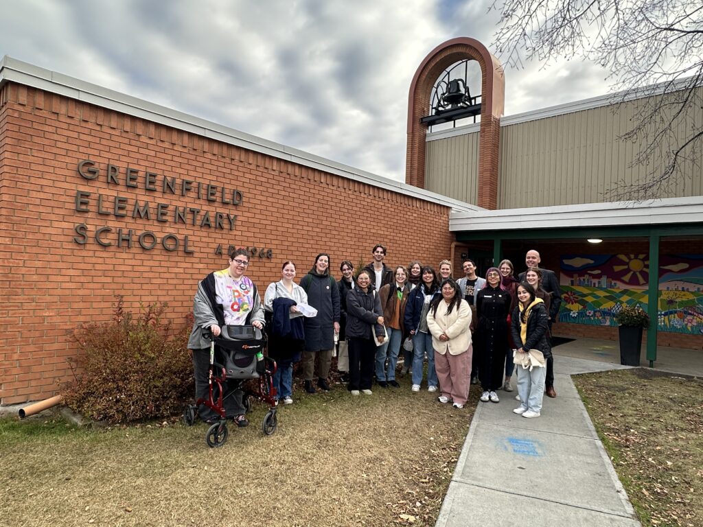 A dozen people in front of a brick school with a bell on top.