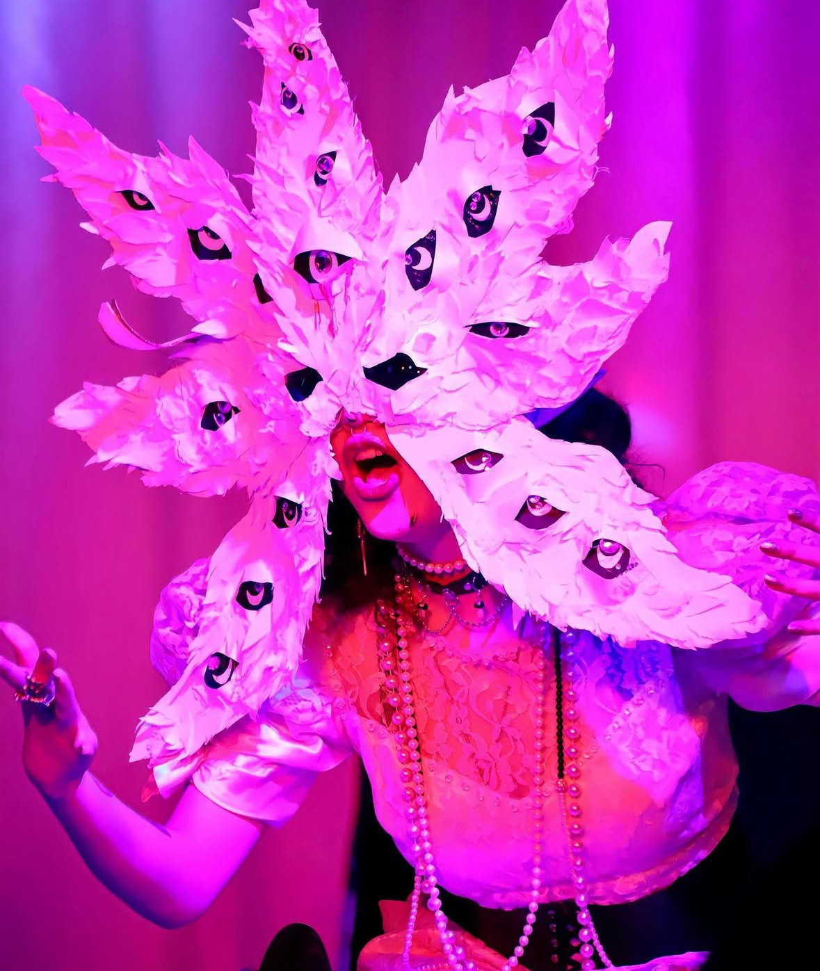 Hot Wheelz lip syncs on stage in a seven-pointed mask with many eyes, which obscures their own eyes.