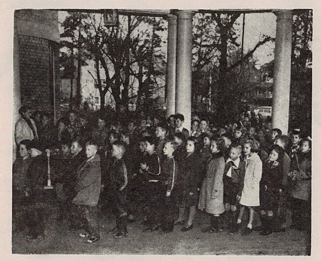 A black and white photograph of a group of schoolchildren lined up outside of an art gallery. Behind them are the pillars of the building’s entrance and a few tall trees.