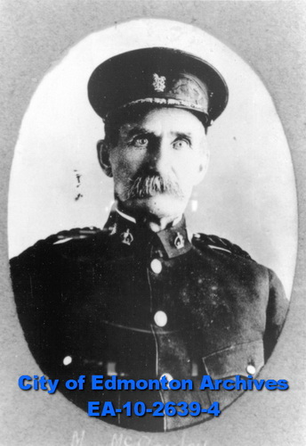 A photograph of a man in uniform with a hat, a high collar, and a thick bushy moustache, spilling over his top lip.