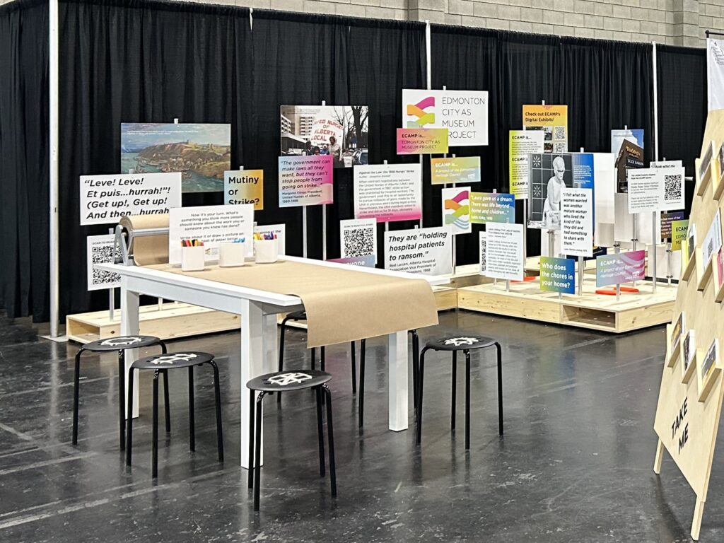 The ECAMP exhibit in Hall B. In the background, a couple dozen exhibit panels look like a rainbow of protest signs. In front, there's a table with a roll of paper and a sign inviting people to write or draw.