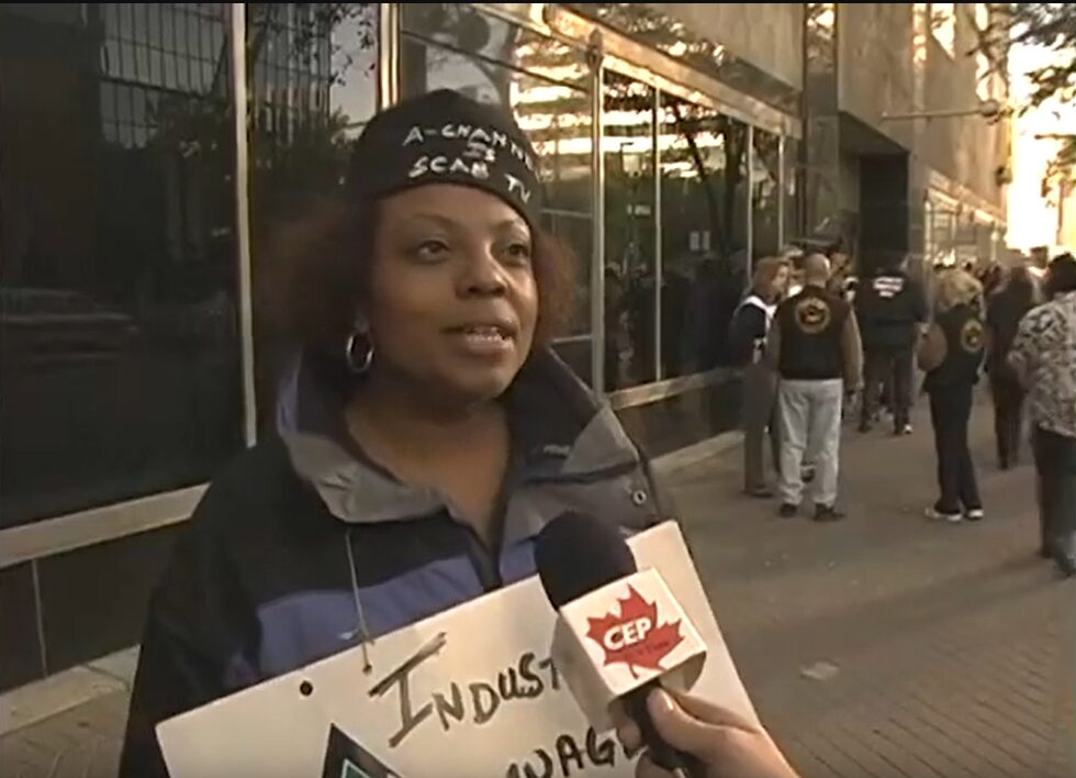 A woman in a toque that says "A-Channel is Scab TV" being interviewed on Jasper Ave.