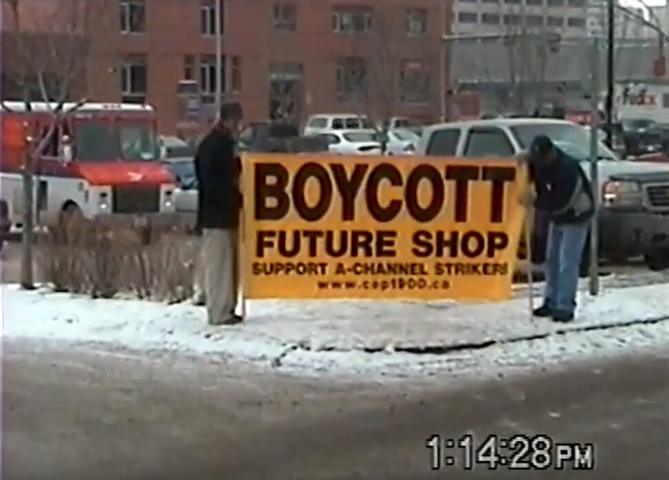 Two people in a snowy parking lot holding up a huge banner that says "Boycott Future Shop: Support A-Channel Strikers."