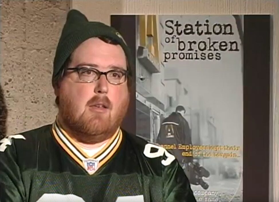 A man in a toque sitting in front of a poster that says "Station of broken promises."