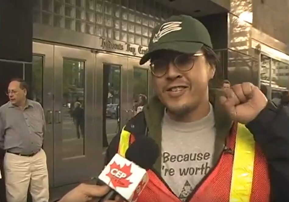 A man in a baseball cap and safety vest enthusiastically raising his left fist while being interviewed on a street corner.